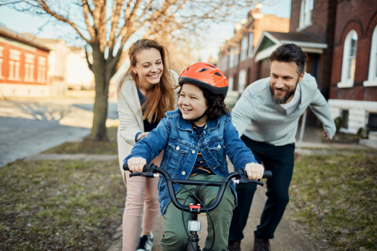 2 parents help a child ride a bike