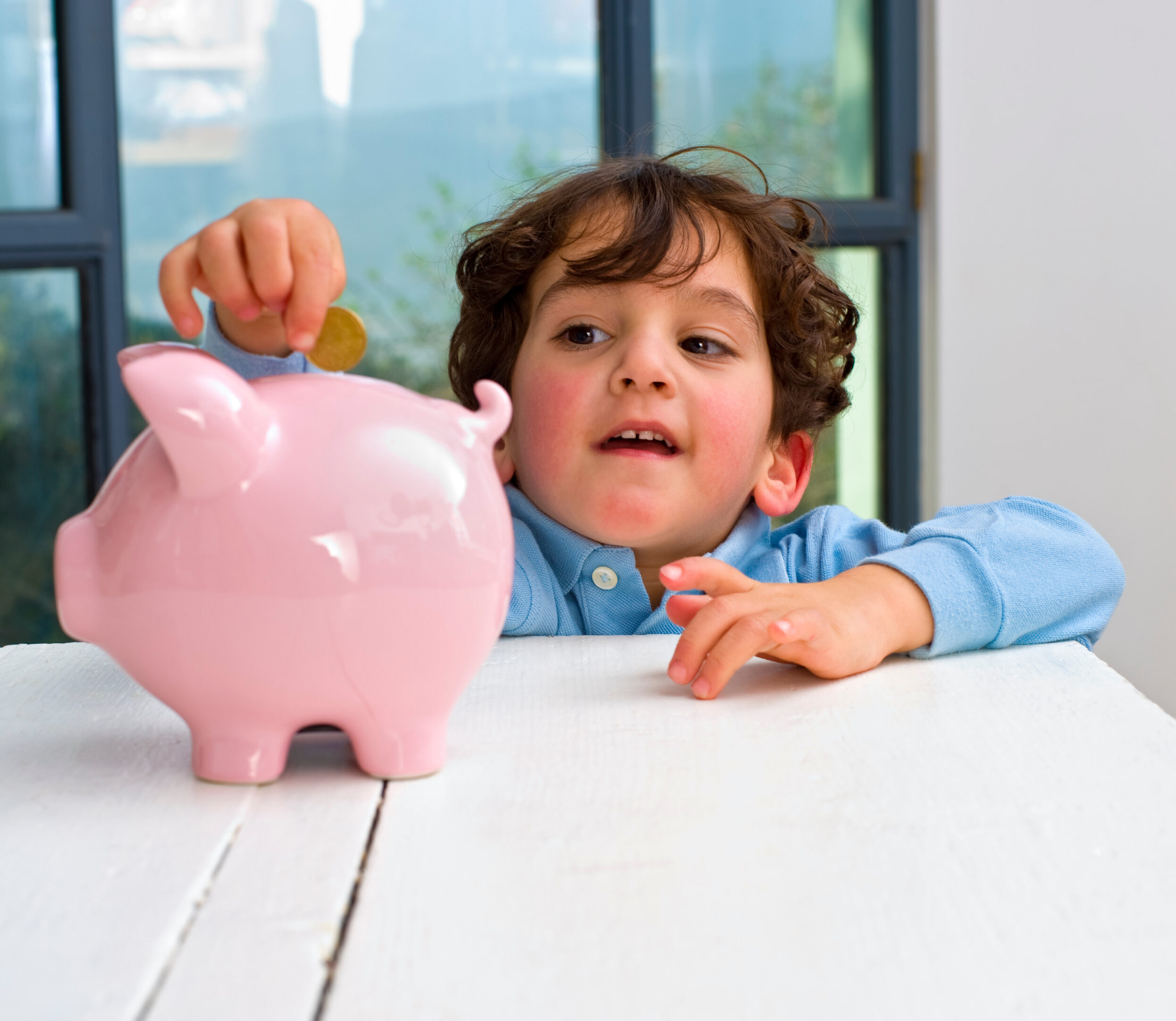 A young boy reaching up to place a coin inside his piggy bank.
