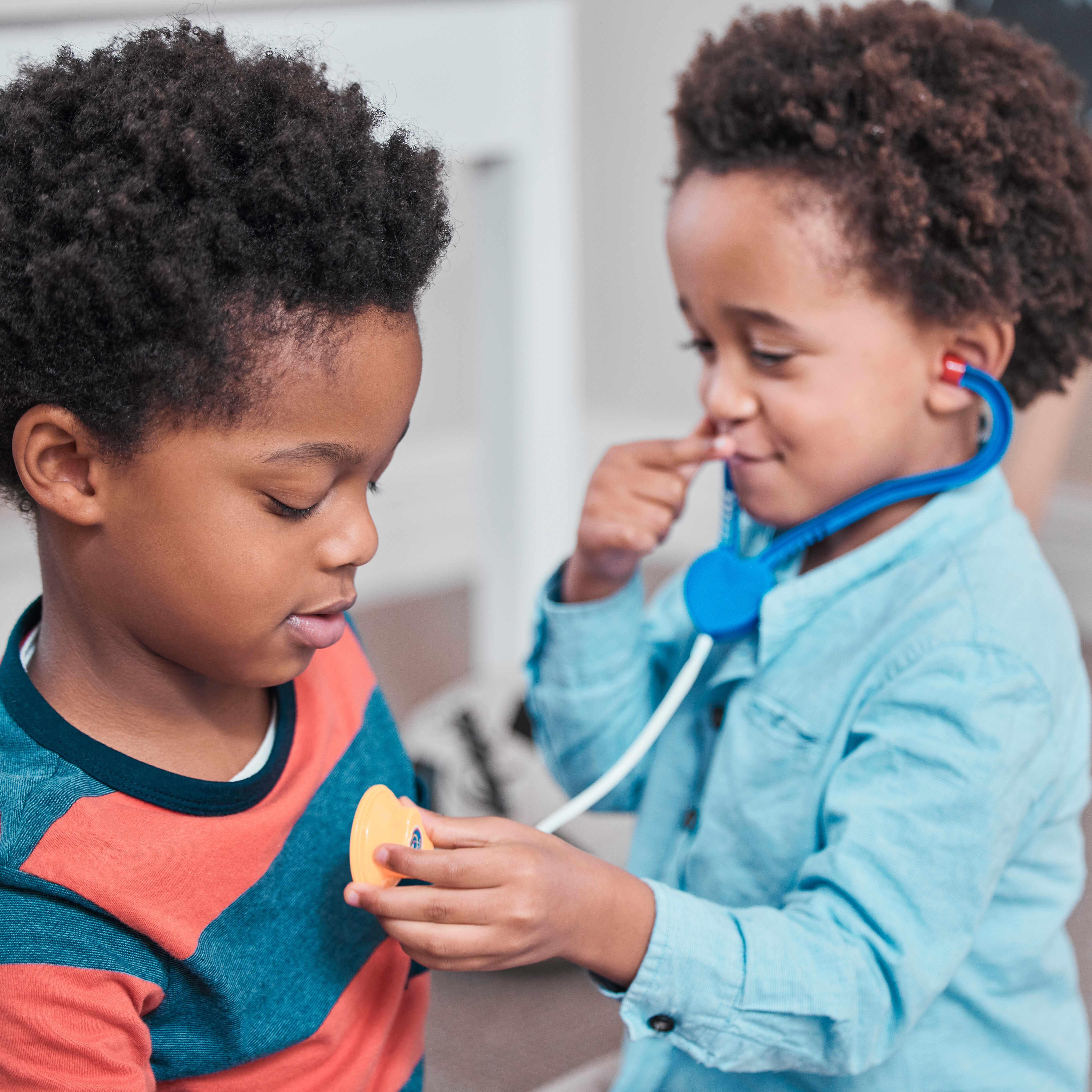 Two brothers playing doctor — one is using a stethoscope to listen to the other's heart.