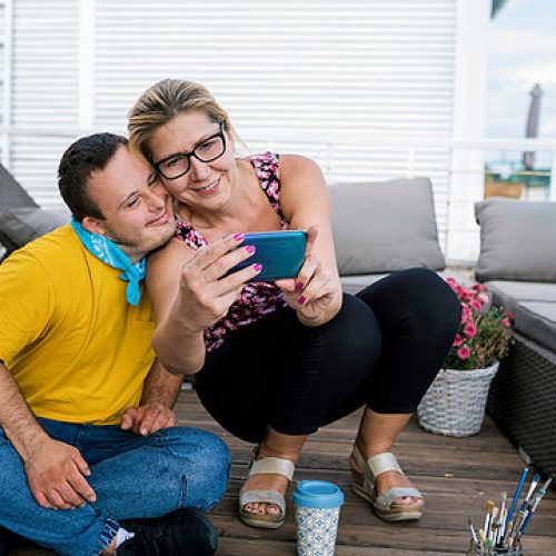 woman-and-man-sitting-on-floor-taking-selfie-adults-with-disabilities-shared-living Woman and man sitting on a floor taking a selfie