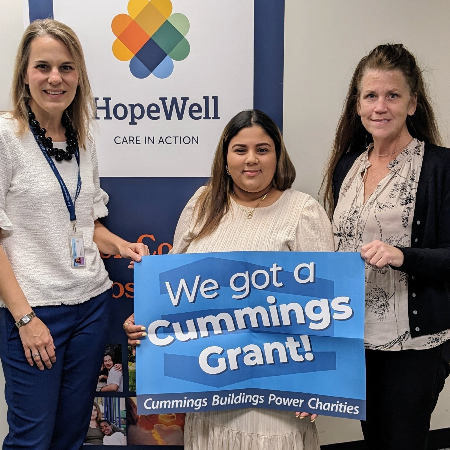 HopeWell team members Lisa Crane, Cristabel Corniel, and Jane Foley hold up a blue sign sharing that HopeWell receiving a Cummings Grant.